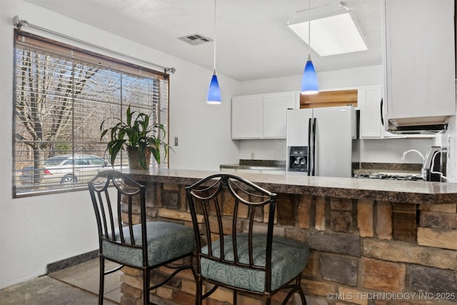 kitchen featuring visible vents, fridge with ice dispenser, hanging light fixtures, and white cabinetry