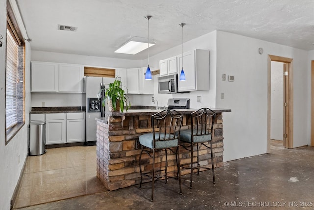 kitchen featuring a breakfast bar, stainless steel appliances, visible vents, hanging light fixtures, and a peninsula