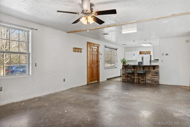 unfurnished living room with a healthy amount of sunlight, a textured ceiling, visible vents, and unfinished concrete flooring