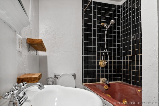 bathroom featuring a sink, a textured wall, bathtub / shower combination, and toilet