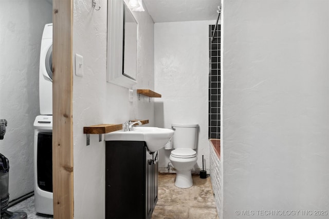 full bath with toilet, a textured wall, stacked washer / dryer, and vanity