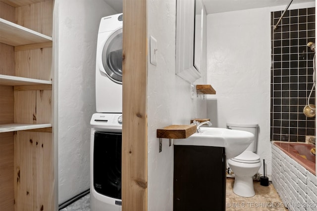 full bathroom featuring toilet, stacked washer and dryer, a textured wall, and vanity