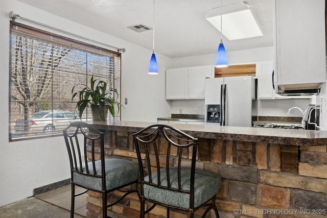 kitchen featuring a kitchen breakfast bar, decorative light fixtures, visible vents, fridge with ice dispenser, and white cabinets