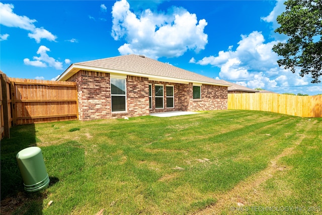 back of property with a shingled roof, brick siding, a yard, and a fenced backyard