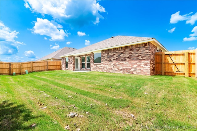 rear view of house featuring brick siding, a yard, and a fenced backyard