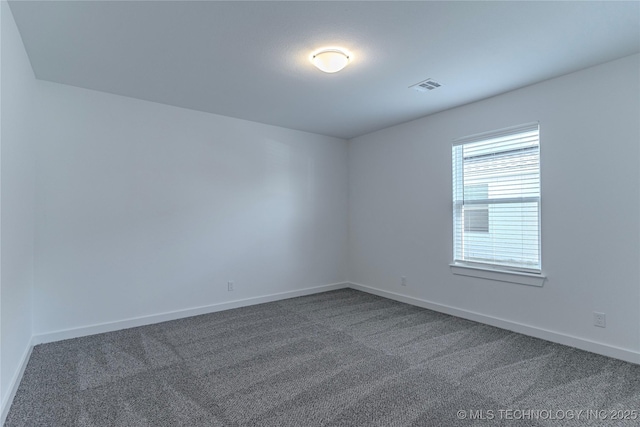 spare room with dark colored carpet, visible vents, and baseboards