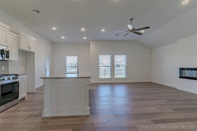 kitchen with a fireplace, light wood finished floors, appliances with stainless steel finishes, white cabinetry, and light stone countertops