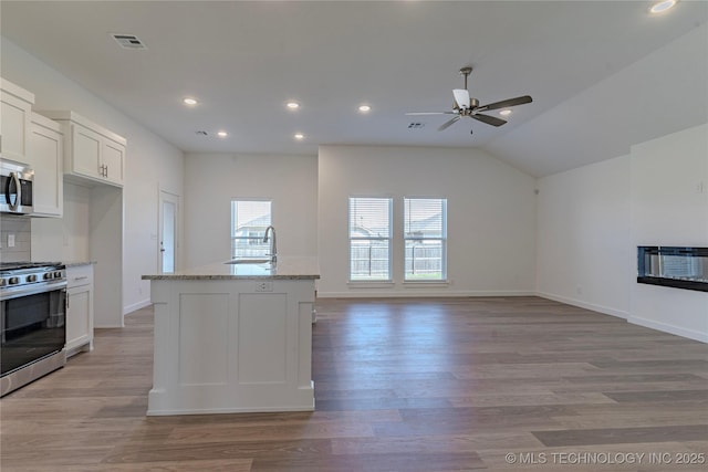 kitchen with stainless steel appliances, a sink, visible vents, white cabinetry, and light stone countertops