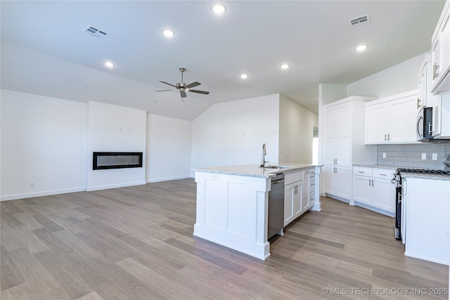 kitchen featuring stainless steel appliances, visible vents, a ceiling fan, a glass covered fireplace, and an island with sink