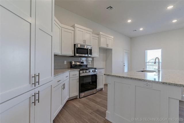 kitchen featuring tasteful backsplash, visible vents, wood finished floors, stainless steel appliances, and a sink