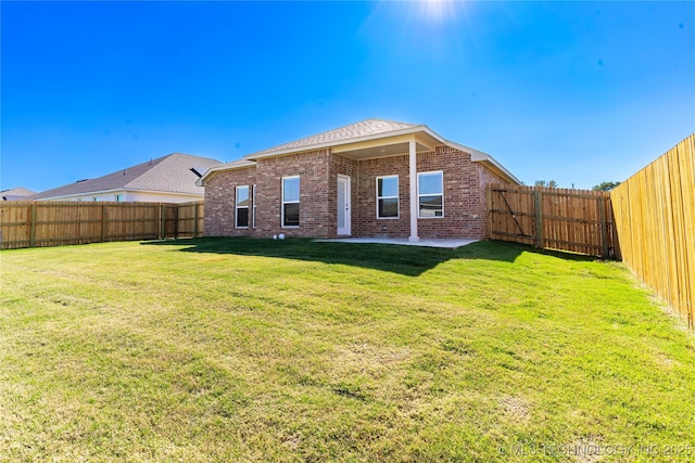 rear view of property featuring a yard, brick siding, a patio area, and a fenced backyard