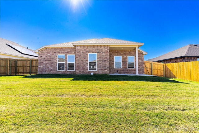 rear view of house featuring brick siding, a yard, a fenced backyard, and a patio