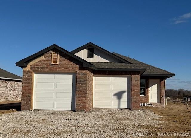 view of front of property with a shingled roof, gravel driveway, brick siding, and an attached garage