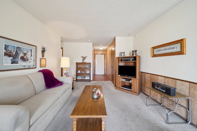 living room featuring light carpet, a wainscoted wall, wooden walls, and a textured ceiling