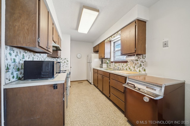 kitchen featuring light countertops, decorative backsplash, freestanding refrigerator, black microwave, and under cabinet range hood