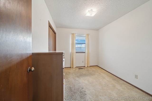 empty room featuring light colored carpet, a textured ceiling, and baseboards