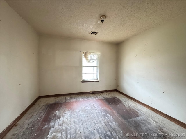 unfurnished room featuring hardwood / wood-style floors, visible vents, and baseboards