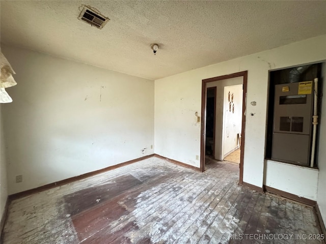 empty room featuring visible vents, a textured ceiling, and baseboards