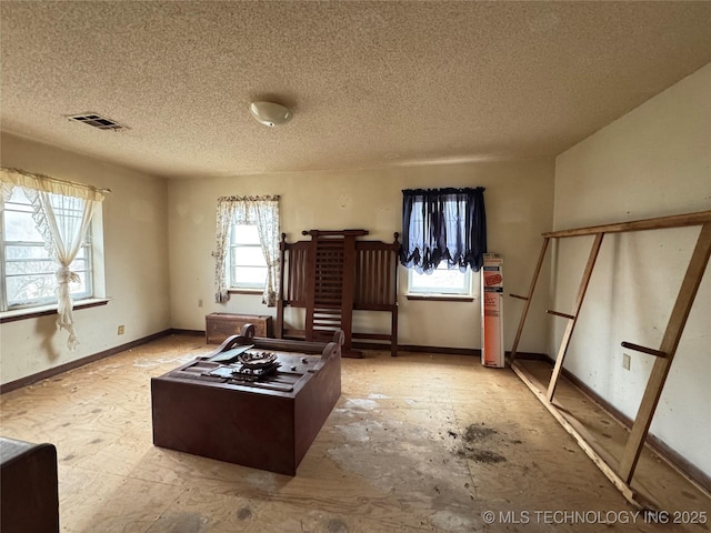 interior space with baseboards, a textured ceiling, visible vents, and a healthy amount of sunlight