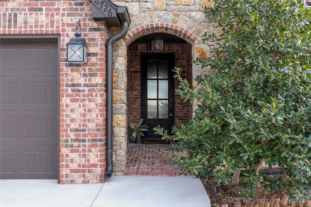 property entrance with a garage, stone siding, and brick siding