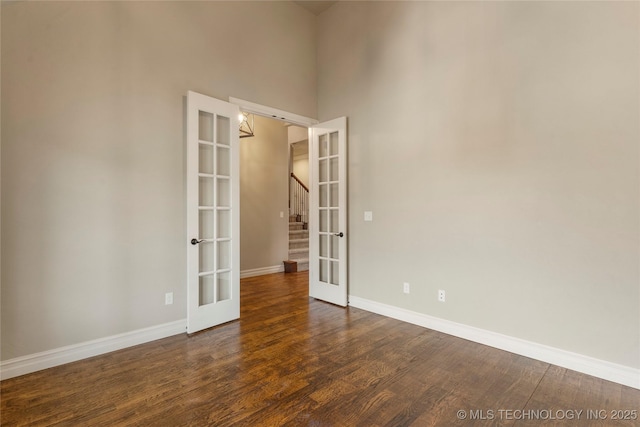 unfurnished room with french doors, a towering ceiling, a barn door, dark wood-type flooring, and baseboards