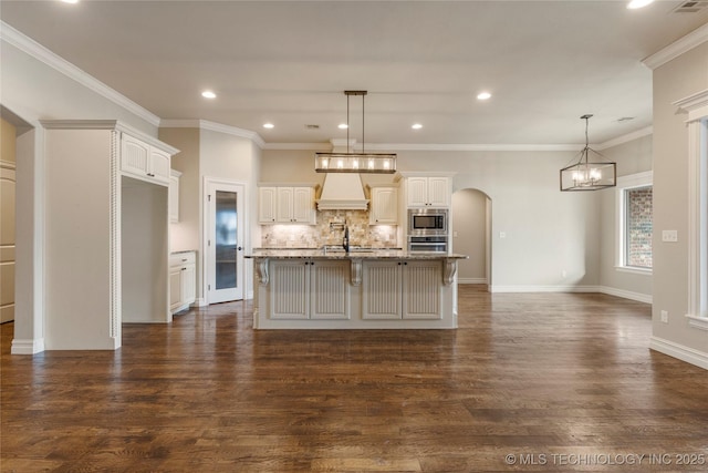 kitchen featuring arched walkways, decorative backsplash, appliances with stainless steel finishes, a sink, and premium range hood