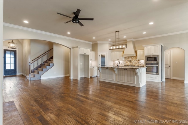 kitchen featuring arched walkways, stainless steel appliances, premium range hood, dark wood-type flooring, and a kitchen bar