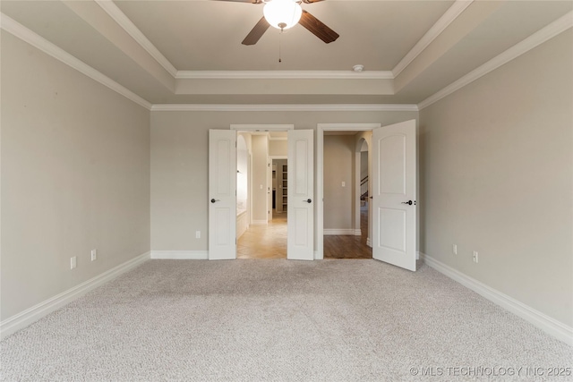 unfurnished bedroom with a tray ceiling, light colored carpet, crown molding, and baseboards