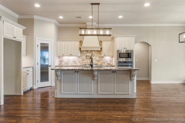 kitchen featuring arched walkways, appliances with stainless steel finishes, light stone countertops, and custom range hood