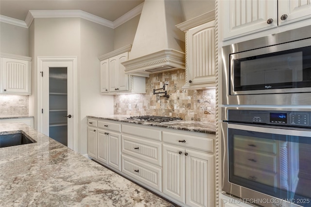 kitchen featuring stainless steel appliances, custom range hood, crown molding, and light stone countertops