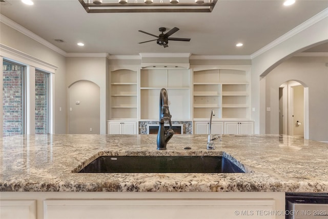 kitchen featuring arched walkways, crown molding, a sink, and light stone countertops