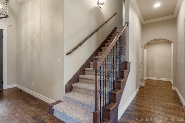 stairs featuring arched walkways, ornamental molding, wood finished floors, and baseboards