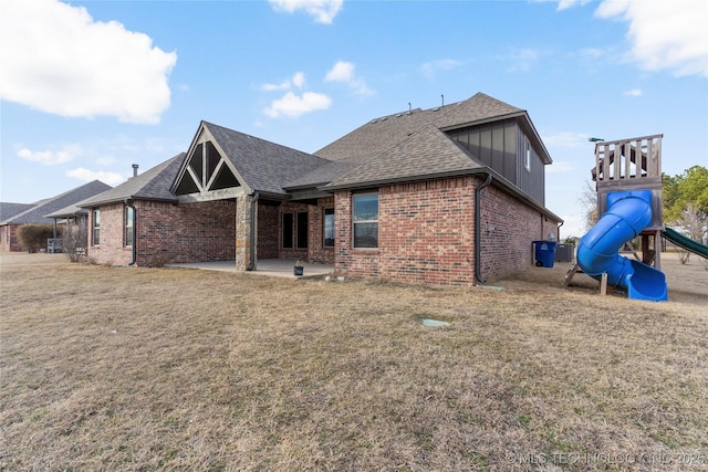 rear view of property with a patio area, a yard, brick siding, and a playground