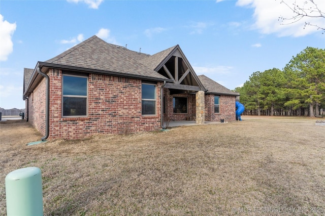 back of property featuring a shingled roof, brick siding, a yard, and a patio