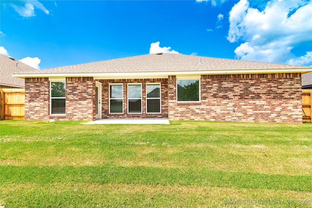 back of property with a patio, brick siding, fence, roof with shingles, and a lawn