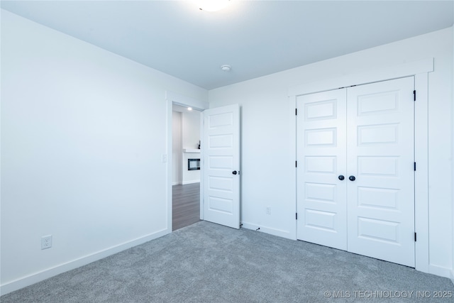 unfurnished bedroom with a glass covered fireplace, a closet, carpet flooring, and baseboards