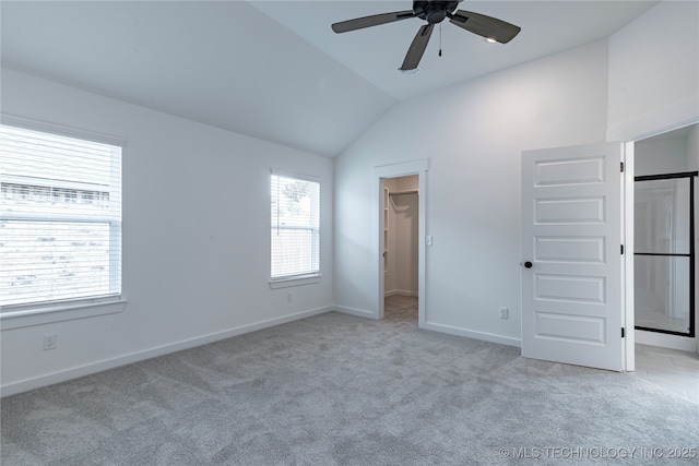 unfurnished bedroom with light colored carpet, baseboards, vaulted ceiling, a spacious closet, and a closet