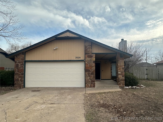 view of front facade featuring a garage, driveway, a chimney, and stone siding