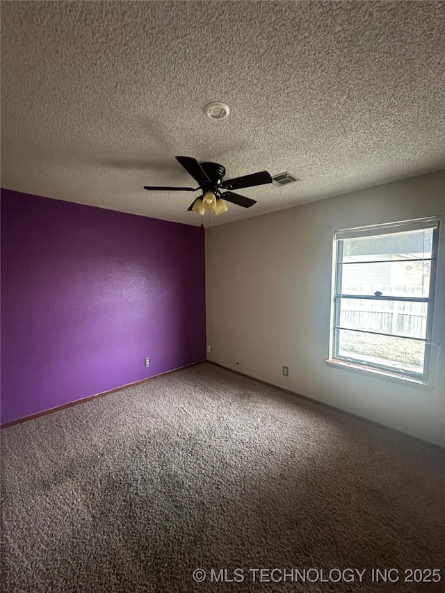 empty room featuring ceiling fan, a textured ceiling, visible vents, and carpet flooring