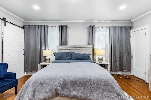 bedroom featuring ornamental molding, wood finished floors, multiple windows, and a barn door