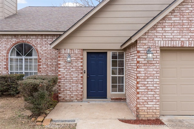 entrance to property with brick siding, a chimney, an attached garage, and roof with shingles