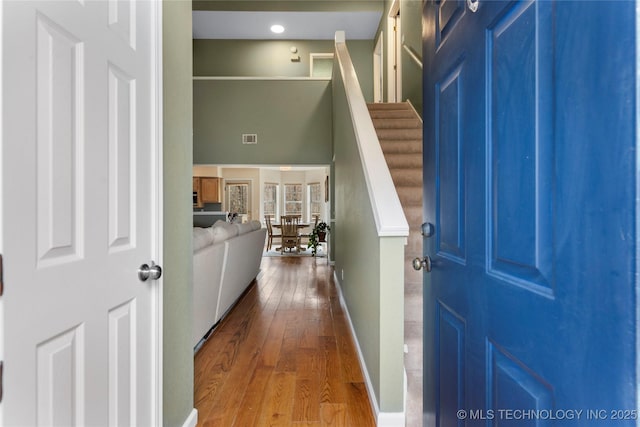 foyer featuring baseboards, visible vents, hardwood / wood-style flooring, stairway, and a high ceiling