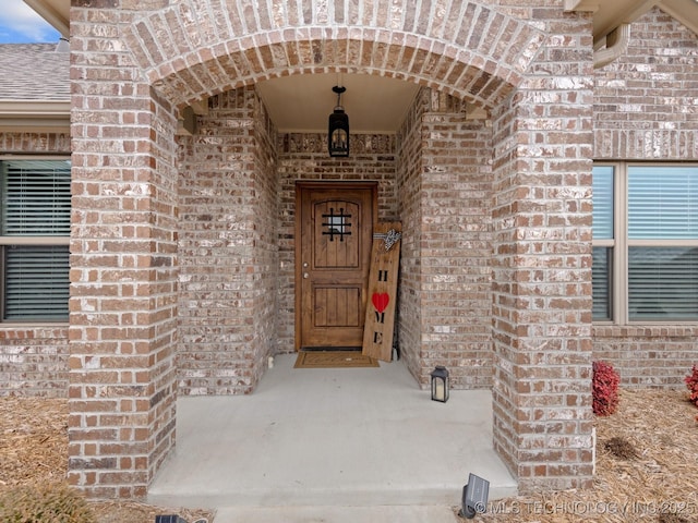 property entrance featuring brick siding and a shingled roof