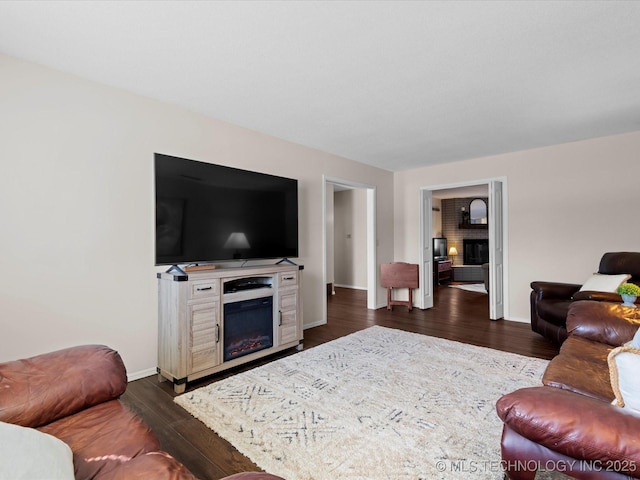 living area with a glass covered fireplace, dark wood-style floors, and baseboards