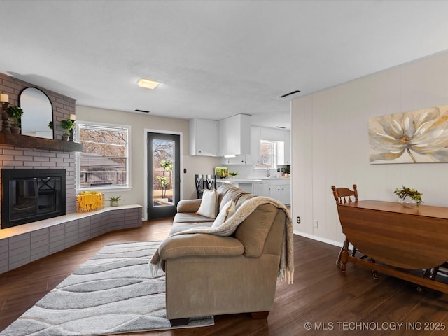 living room featuring visible vents, a brick fireplace, and dark wood-style flooring