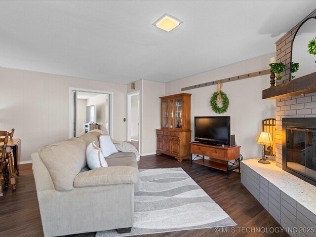 living room with dark wood finished floors, a brick fireplace, and baseboards