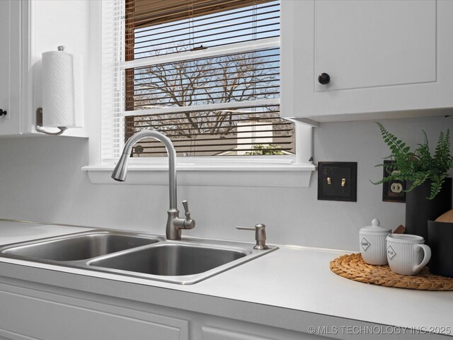 interior details with a sink, white cabinetry, and light countertops