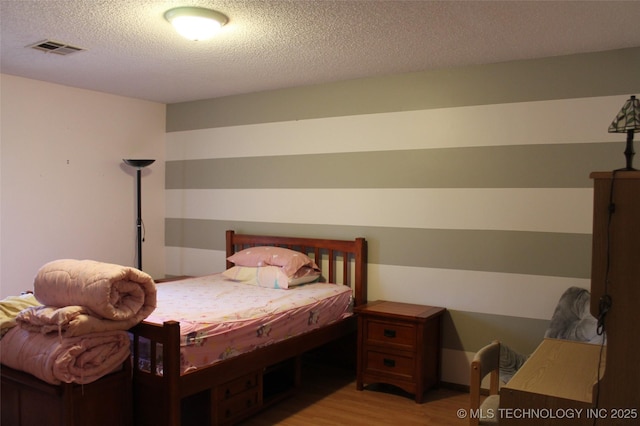 bedroom featuring light wood finished floors, visible vents, and a textured ceiling