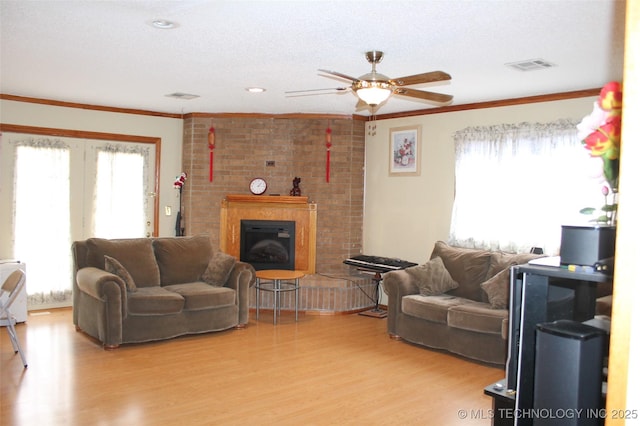 living area featuring light wood-style floors, a wealth of natural light, visible vents, and ornamental molding