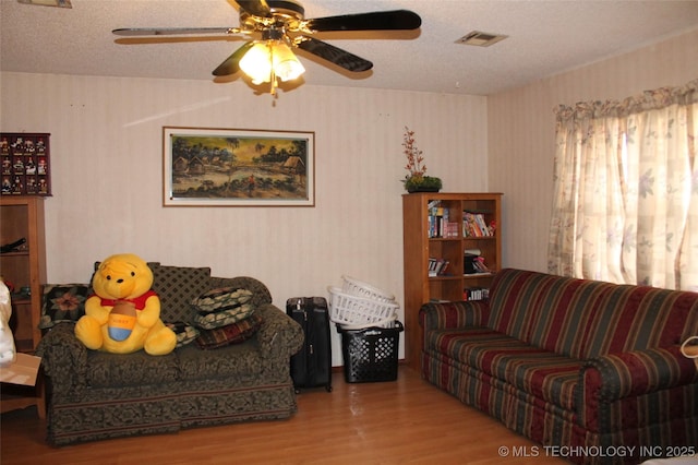 living room with a textured ceiling, ceiling fan, wood finished floors, visible vents, and wallpapered walls